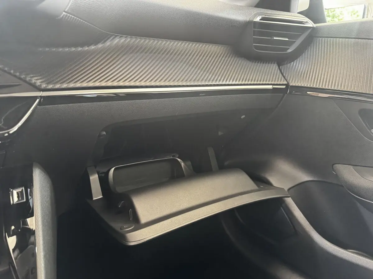 Vue intérieure côté passager de la Peugeot 208 2020, boîte à gants ouverte et tableau de bord noir avec insert effet carbone.