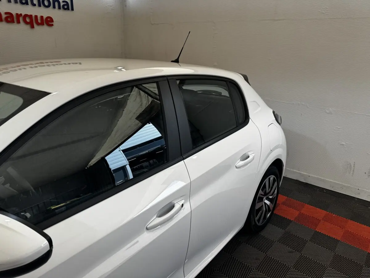 Vue côté droit arrière d'une Peugeot 208 blanche garée sur un sol à damiers noir et rouge, en intérieur.