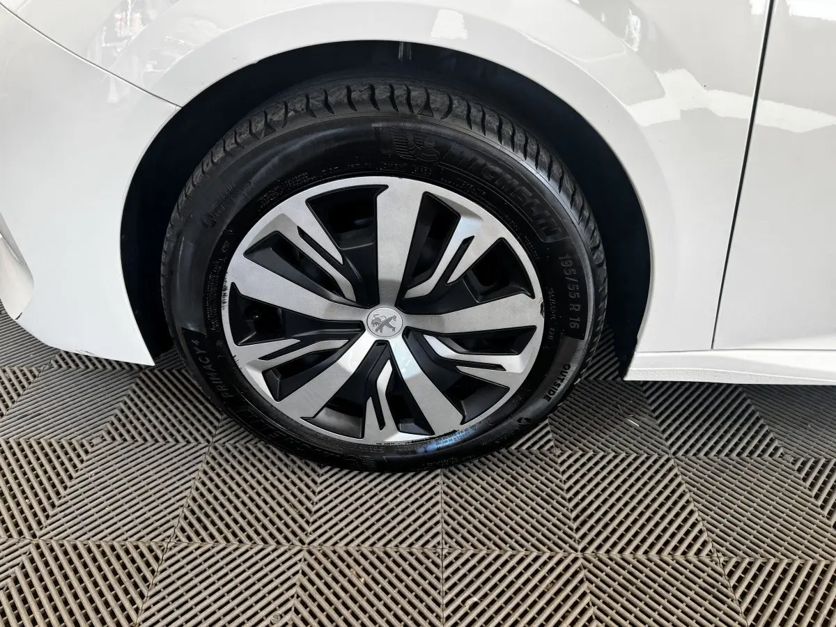 Gros plan sur la roue avant gauche d’une Peugeot 208 blanche avec jante alliage au design moderne.