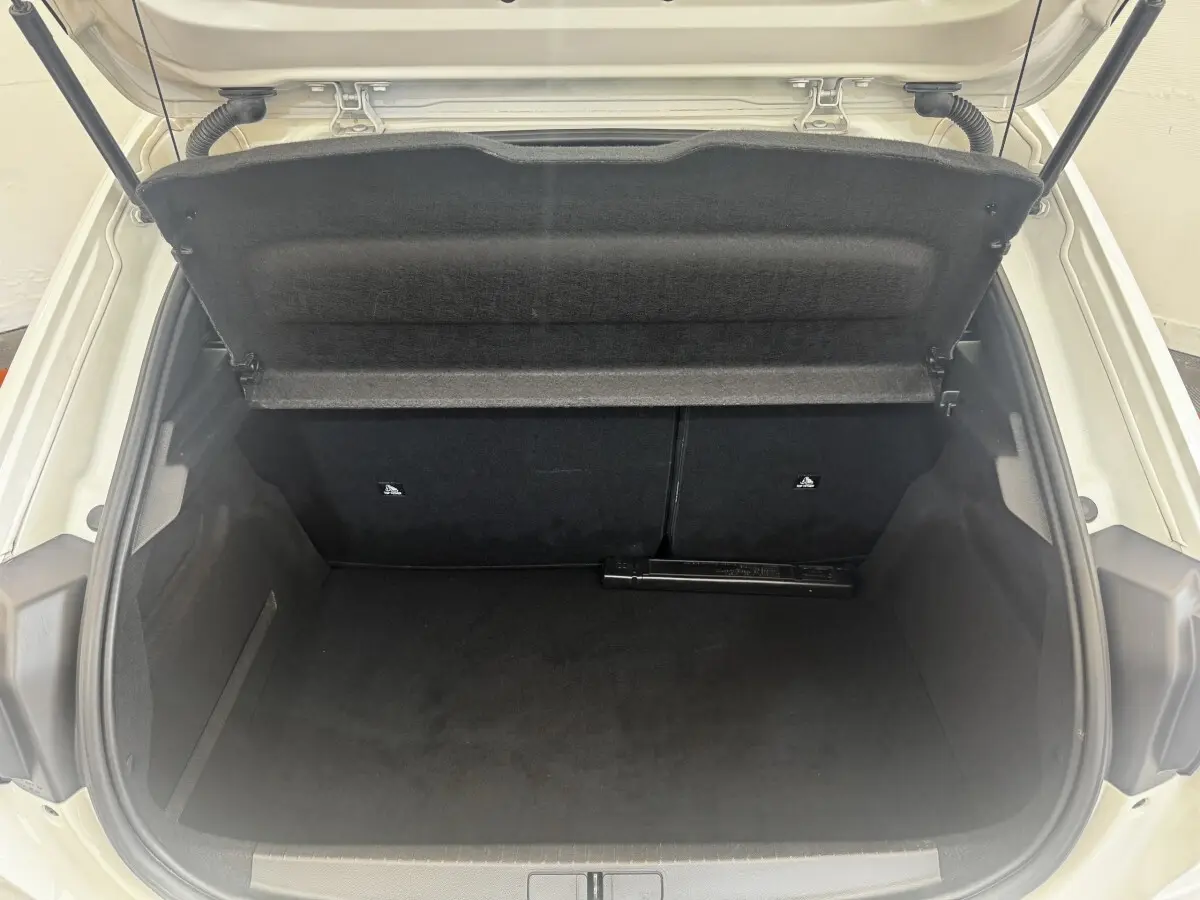 Coffre ouvert vu de l'arrière d'une Peugeot 208 blanche, montrant l'espace de chargement vide et la tablette de séparation.