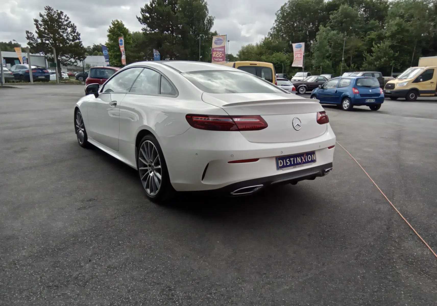 Vue 3/4 arrière gauche d'une Mercedes Classe E Coupé blanche AMG Line avec jantes alliage et feux LED distinctifs.