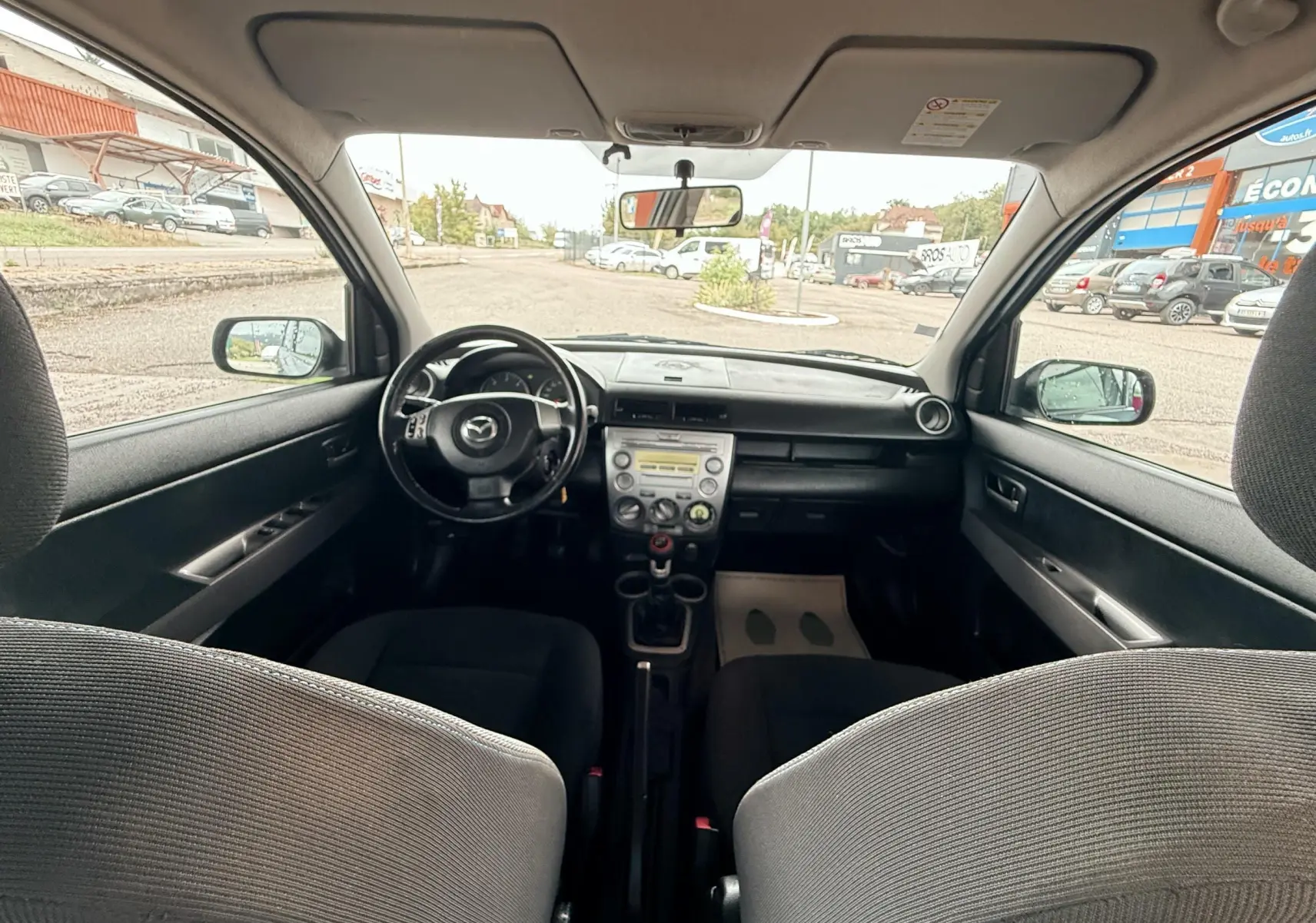 Intérieur noir de la Mazda2 2004 vu de l'arrière, avec tableau de bord et volant au centre.