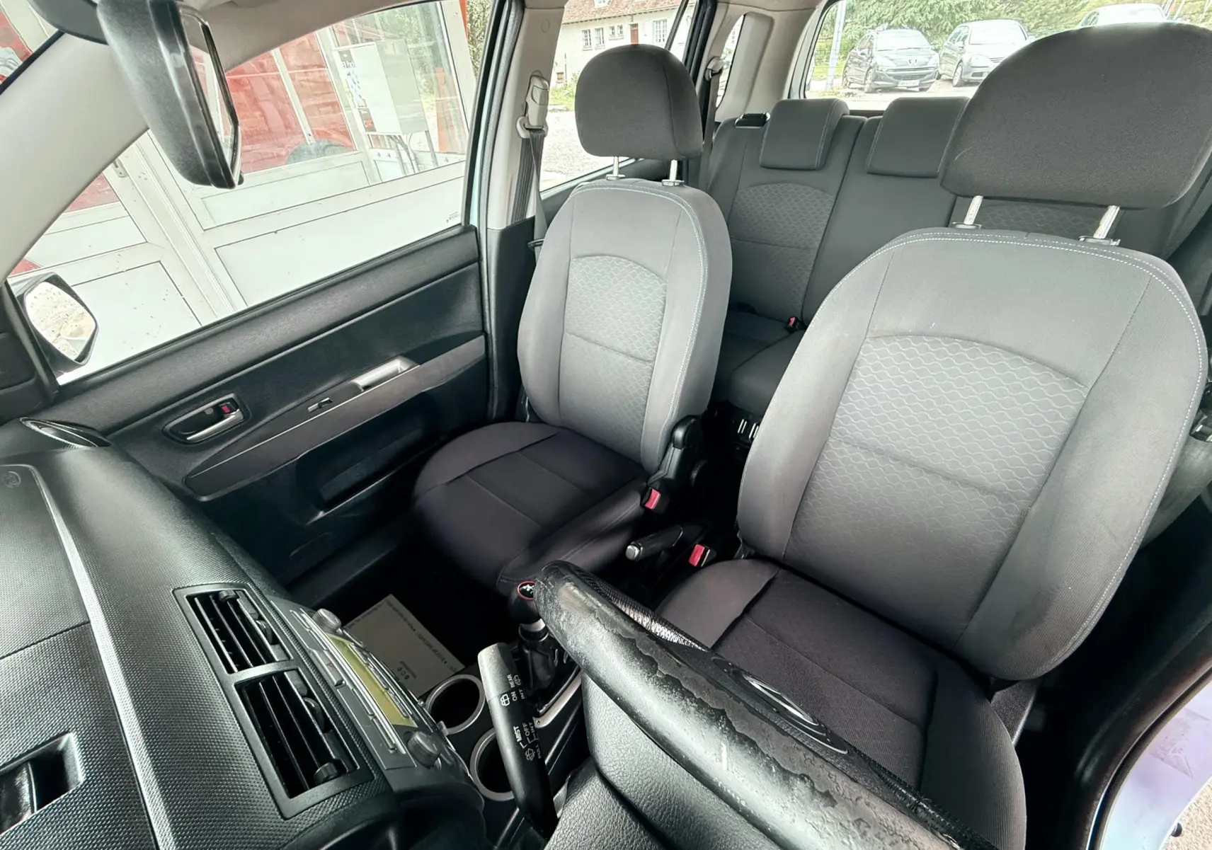 Intérieur de la Mazda2 2004 montrant les sièges avant en tissu noir et gris, vue côté conducteur ouverte.