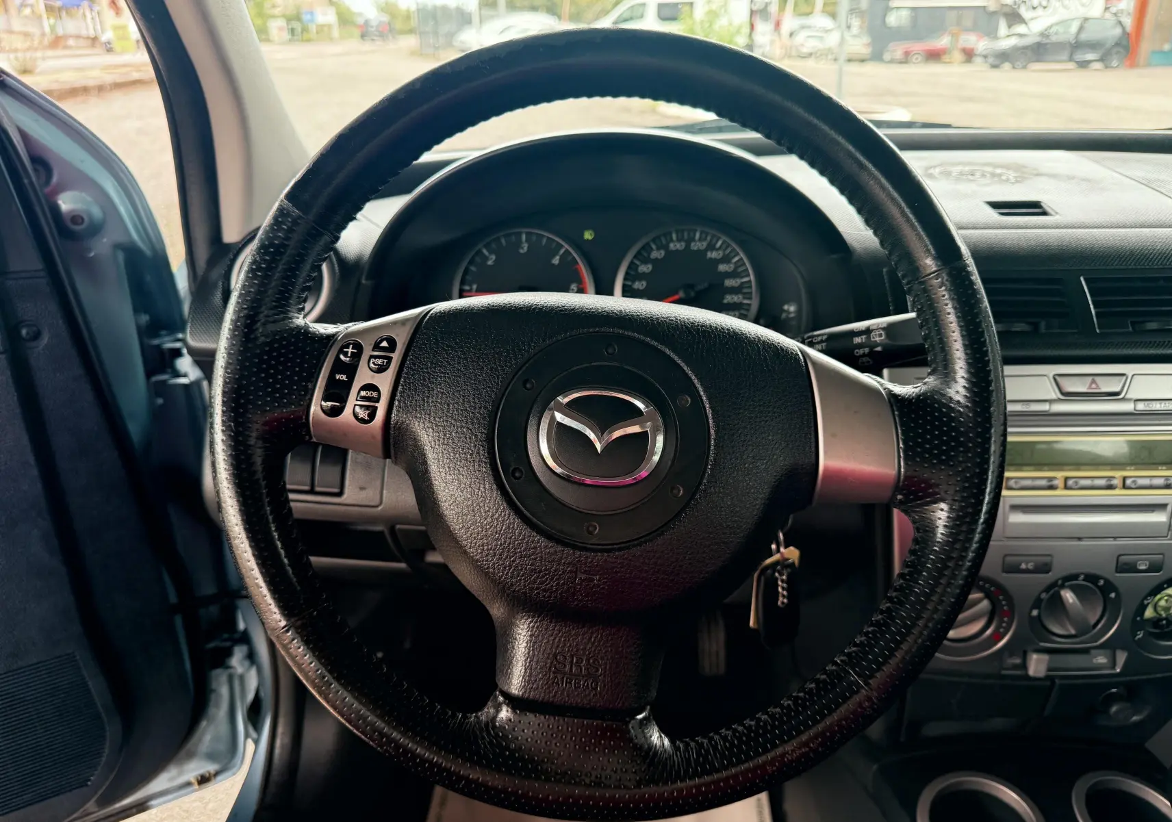 Volant en cuir noir avec logo Mazda au centre, tableau de bord et console centrale d'une Mazda2 gris vue de l'intérieur côté conducteur.