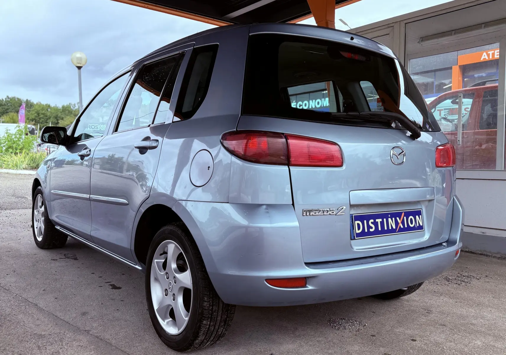 Vue 3/4 arrière gauche d'une Mazda2 gris clair avec hayon et jantes alliage sous un abri.