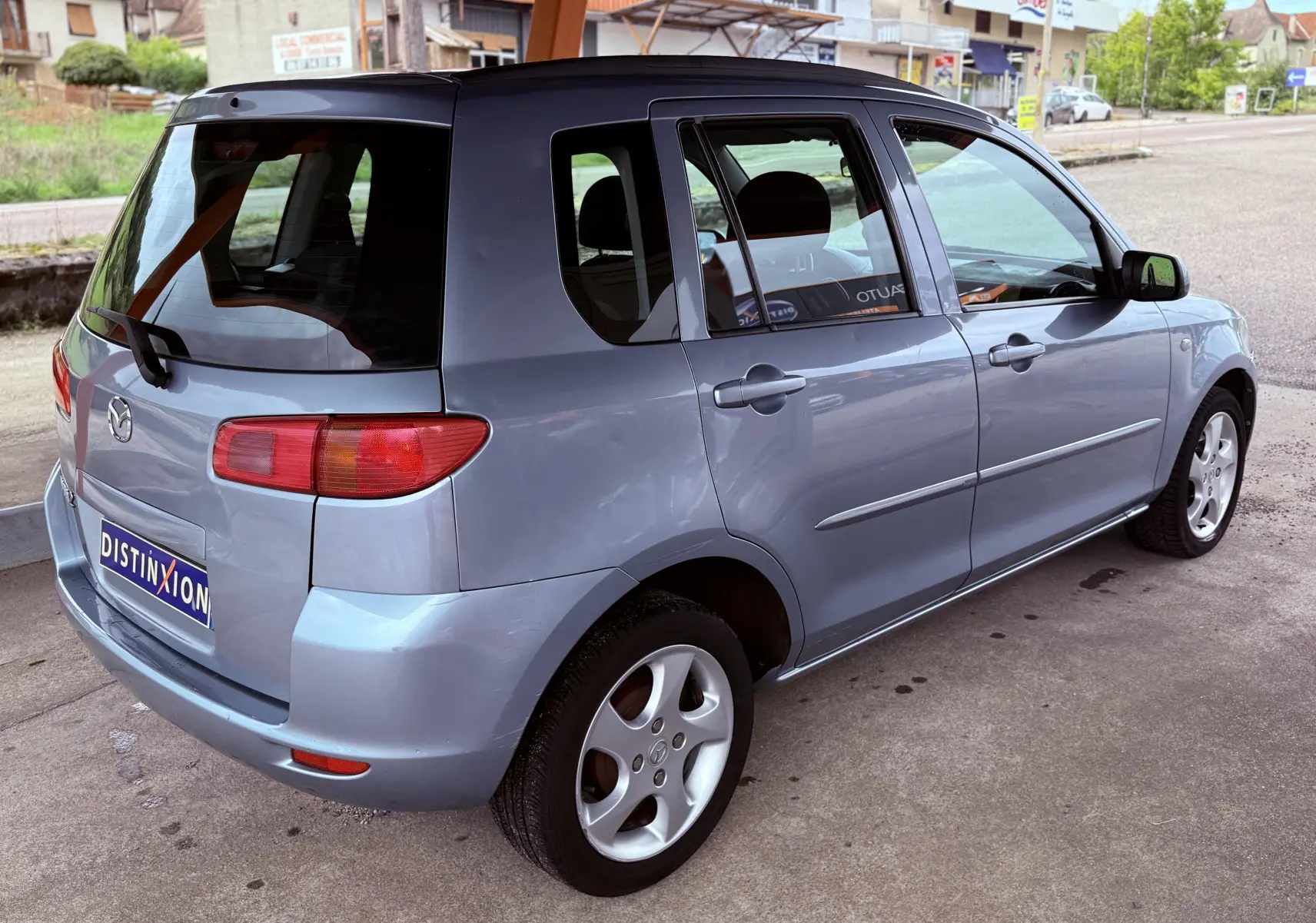 Vue 3/4 arrière droite d'une Mazda2 gris clair de 2004, compacte cinq portes avec jantes alliage et vitres teintées.