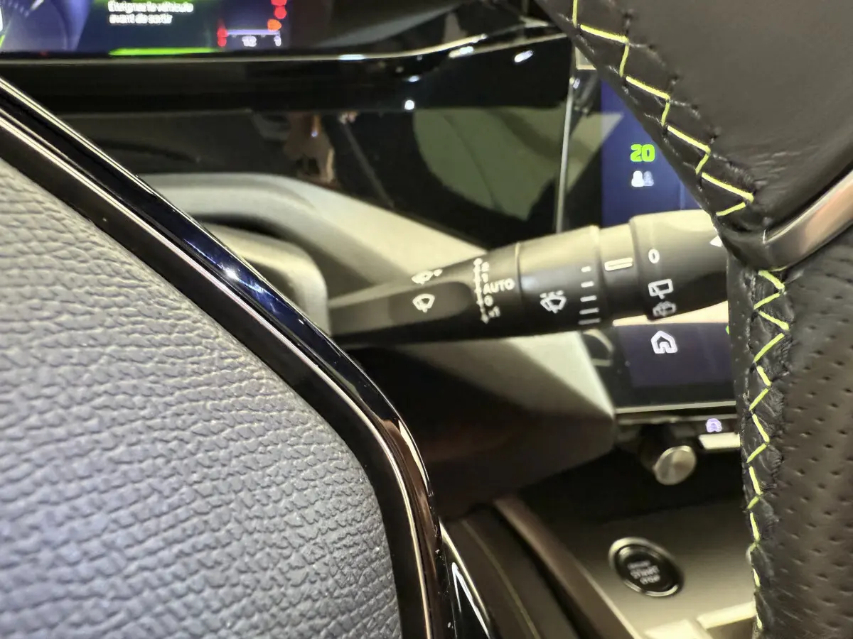 Détail intérieur du volant cuir noir avec surpiqûres vertes et commandes, tableau de bord tactile Peugeot 308 Hybrid 2024.