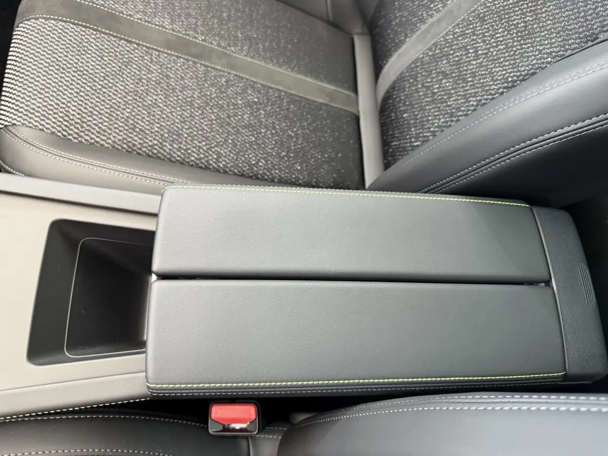 Vue rapprochée de l'accoudoir central noir avec surpiqûres vertes dans l'habitacle de la Peugeot 308 Hybrid 2024.