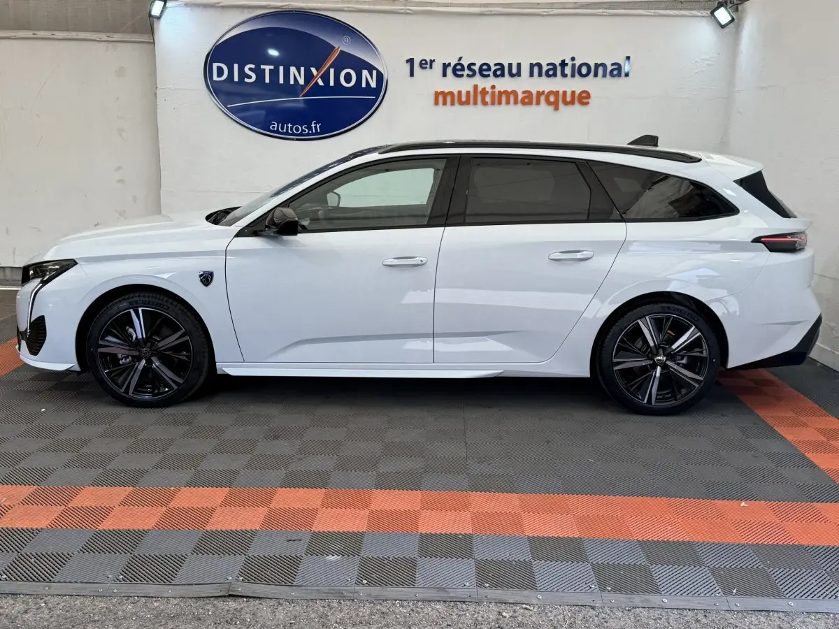 Profil côté gauche d'une Peugeot 308 Hybrid 136 e-DCS6 GT blanche avec jantes noires et toit ouvrant panoramique.
