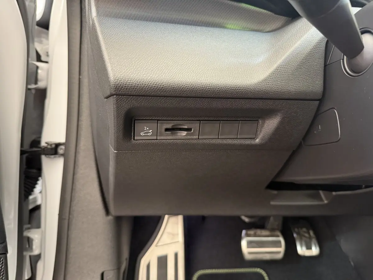 Gros plan sur la commande d'ouverture du coffre côté gauche, intérieur noir, pédales alu visibles, Peugeot 308 blanc 2024.