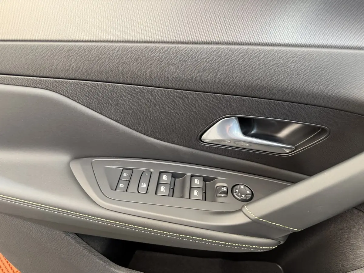 Détail de la porte côté gauche intérieure d'une Peugeot 308 Hybrid blanche, avec commandes vitres et poignée chromée.