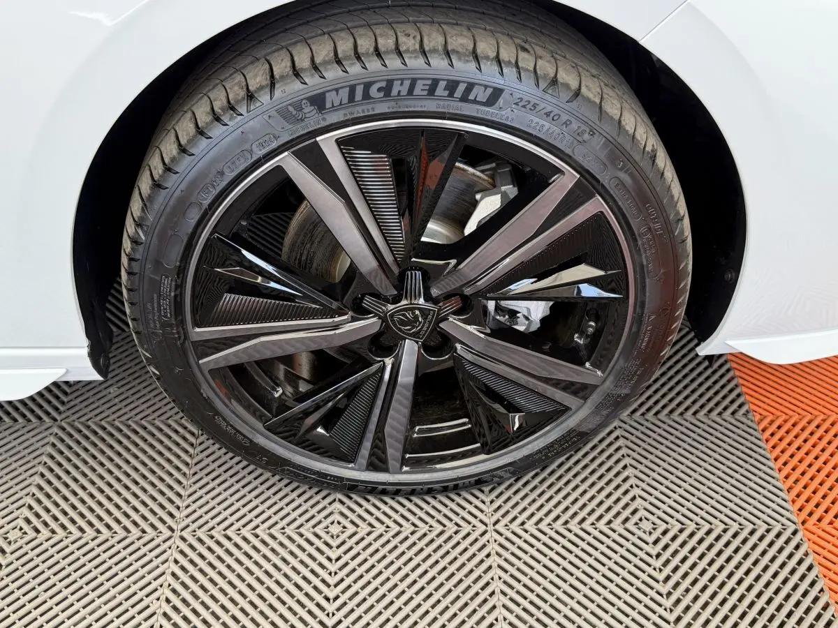 Gros plan sur la roue avant droite de la Peugeot 308 Hybrid 136 e-DCS6 GT blanche avec jante noire brillante au design moderne.