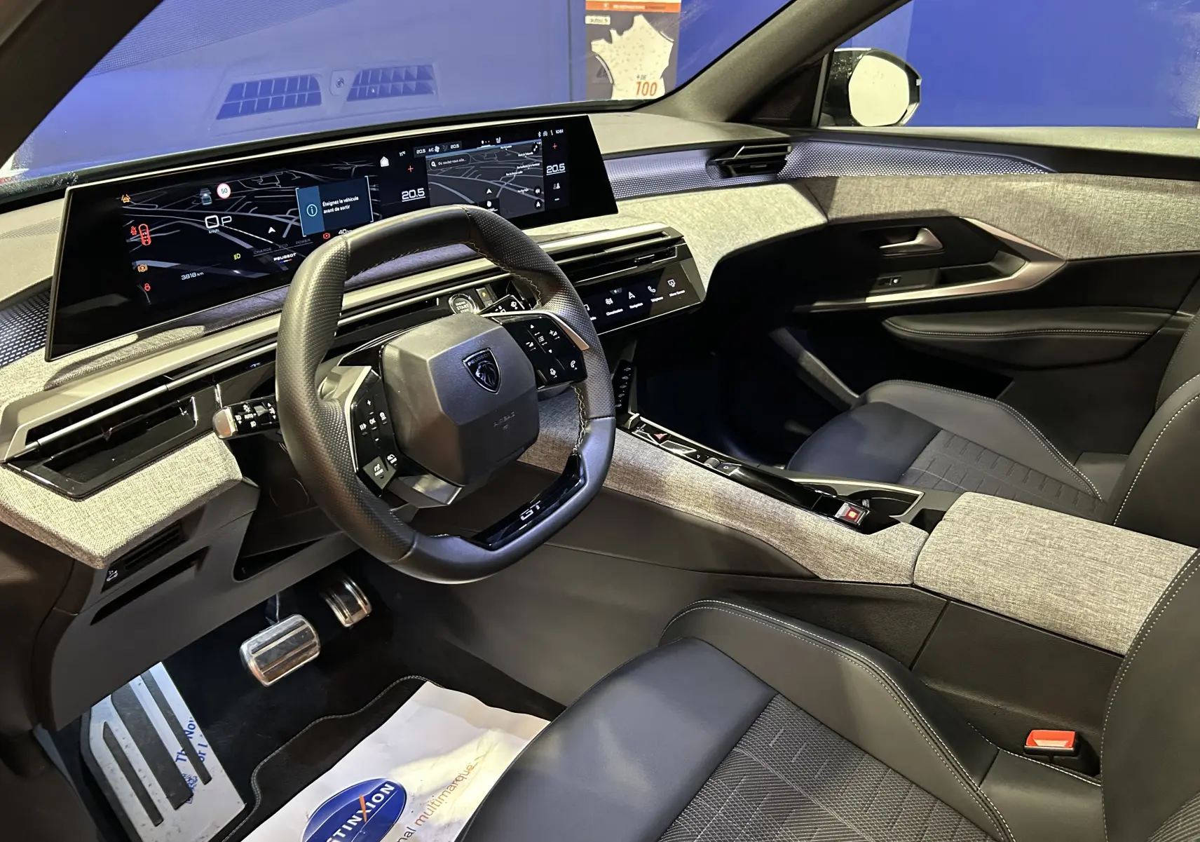 Intérieur du Peugeot 5008 Hybrid 2025 vu côté conducteur, avec tableau de bord numérique et sellerie gris clair et noire.