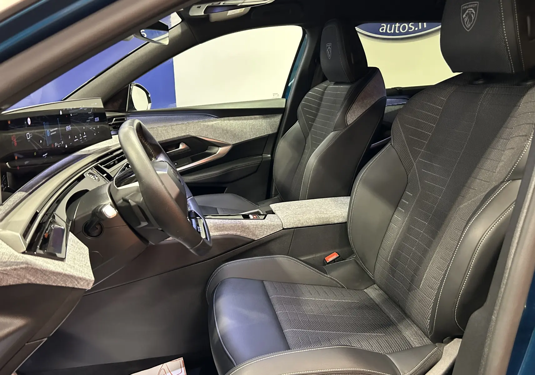 Intérieur du Peugeot 5008 Hybrid 2025 vu côté conducteur, sièges cuir noir avec surpiqûres blanches et tableau de bord moderne.