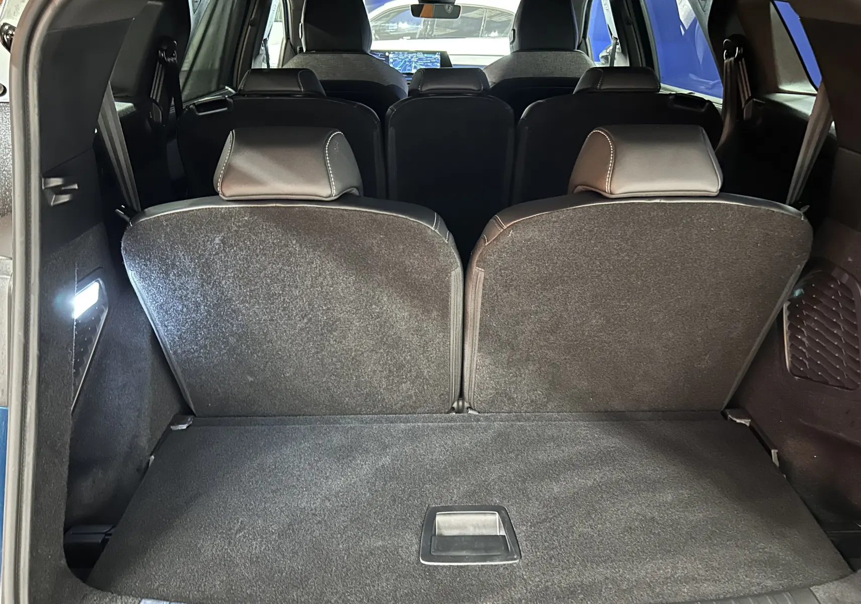 Vue depuis le hayon ouvert du coffre du Peugeot 5008 bleu obsession, montrant la troisième rangée de sièges relevée.