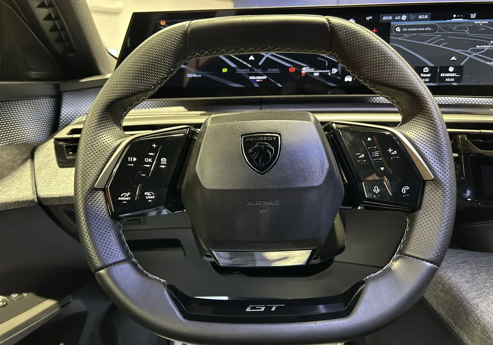 Volant cuir perforé noir avec logo Peugeot et inscription GT, vue frontale du poste de conduite du 5008 Hybrid 2025.