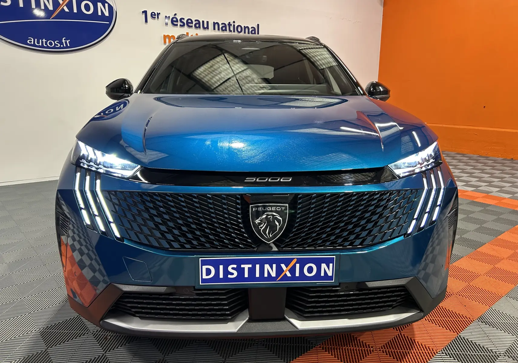 Vue frontale d'un Peugeot 5008 bleu obsession avec calandre noire et feux LED verticaux allumés dans un showroom.