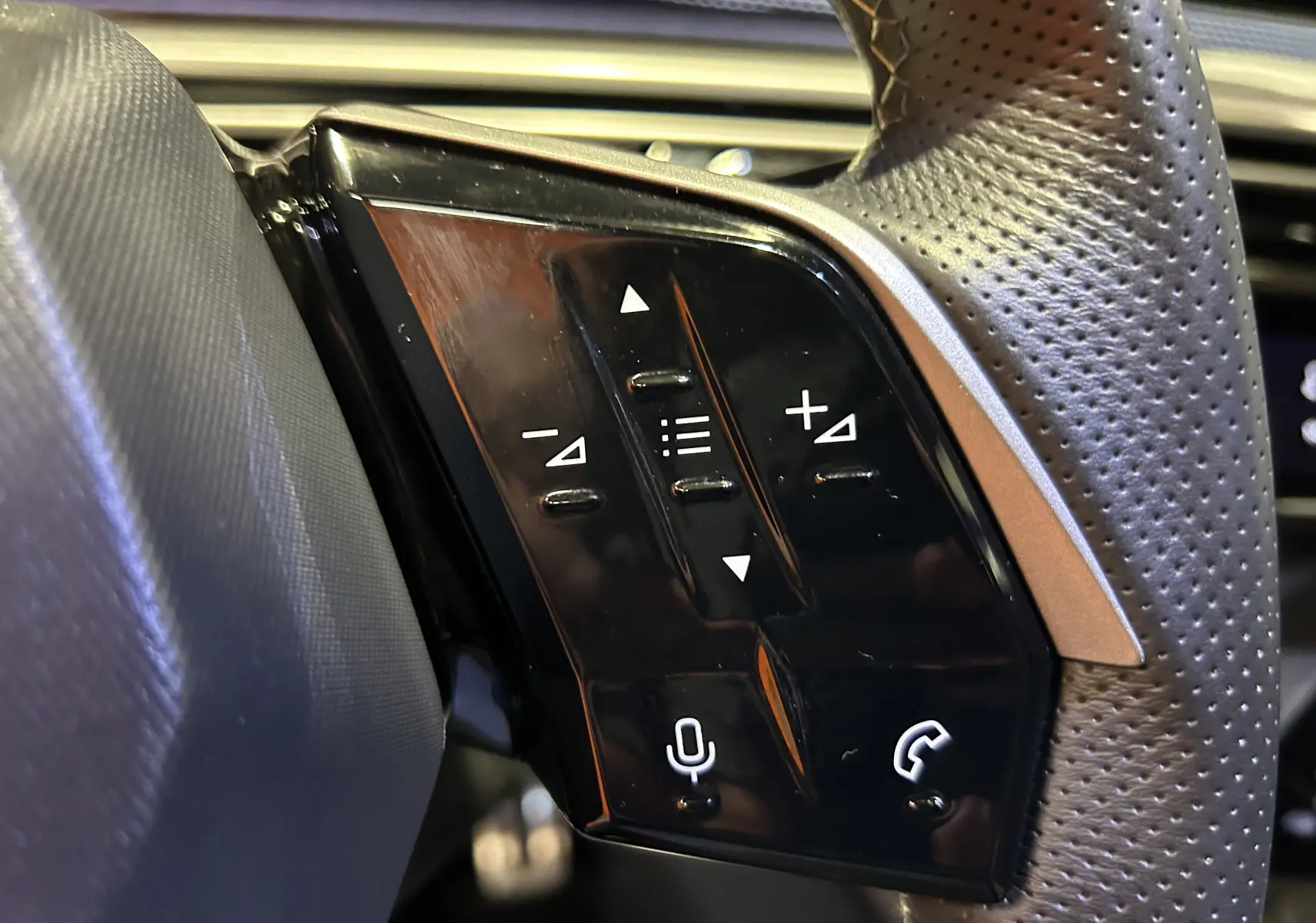 Gros plan sur les commandes noires du volant en cuir perforé du Peugeot 5008 hybride 2025, côté gauche.