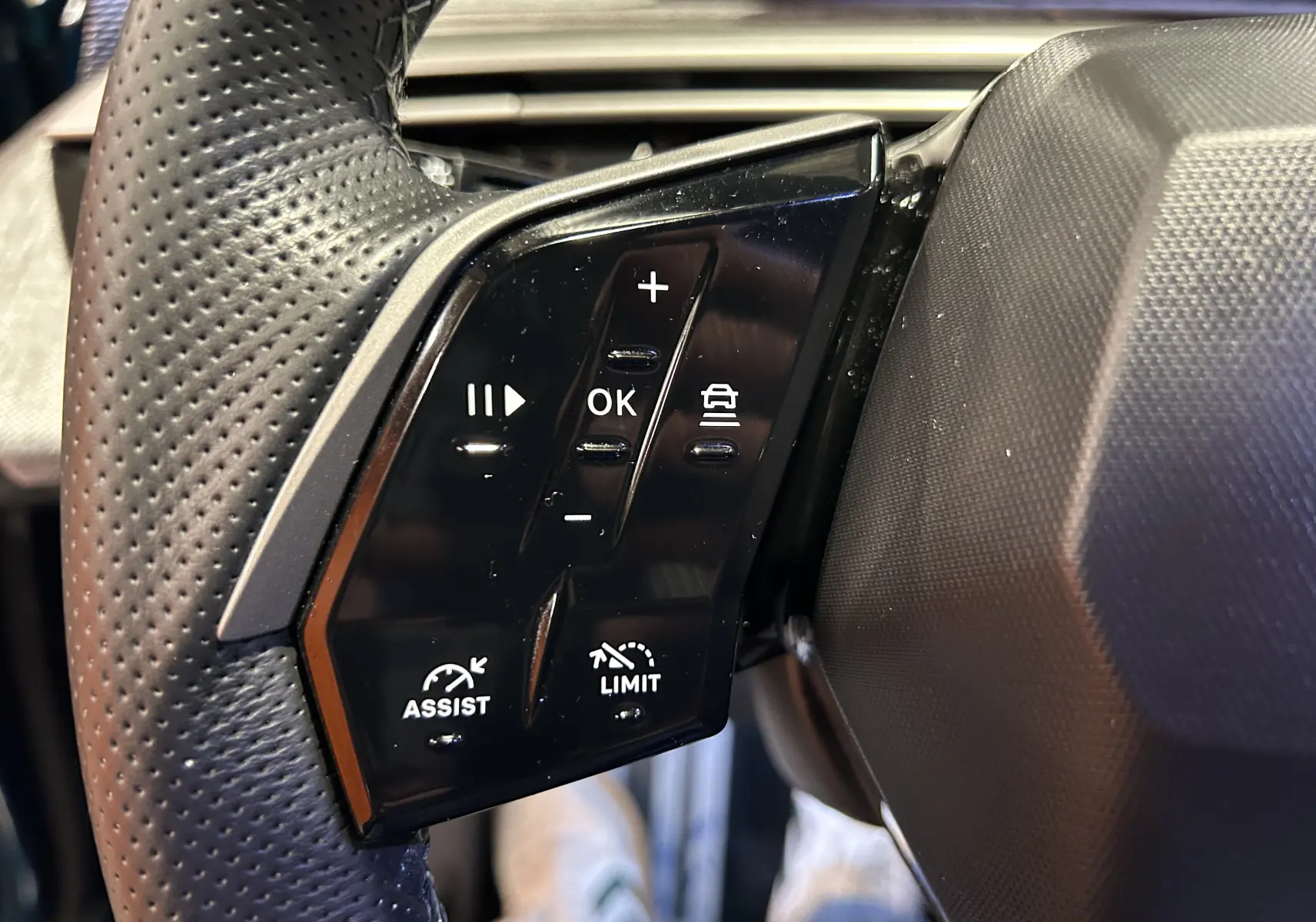 Gros plan sur les commandes du volant à gauche du Peugeot 5008 III Hybrid 145 e-DSC6 GT, finition cuir perforé.