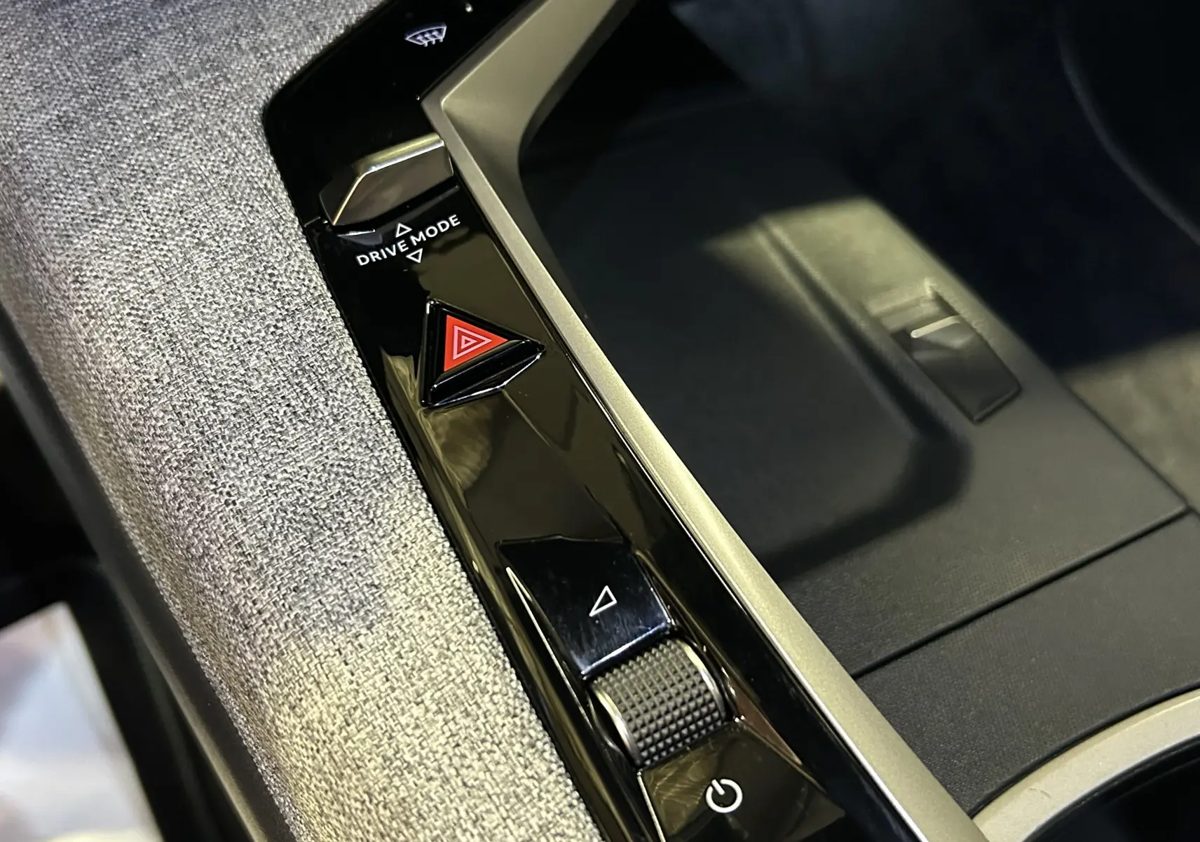Gros plan sur la console centrale du Peugeot 5008 III Hybrid 145 GT avec bouton Drive Mode et tissu gris texturé.