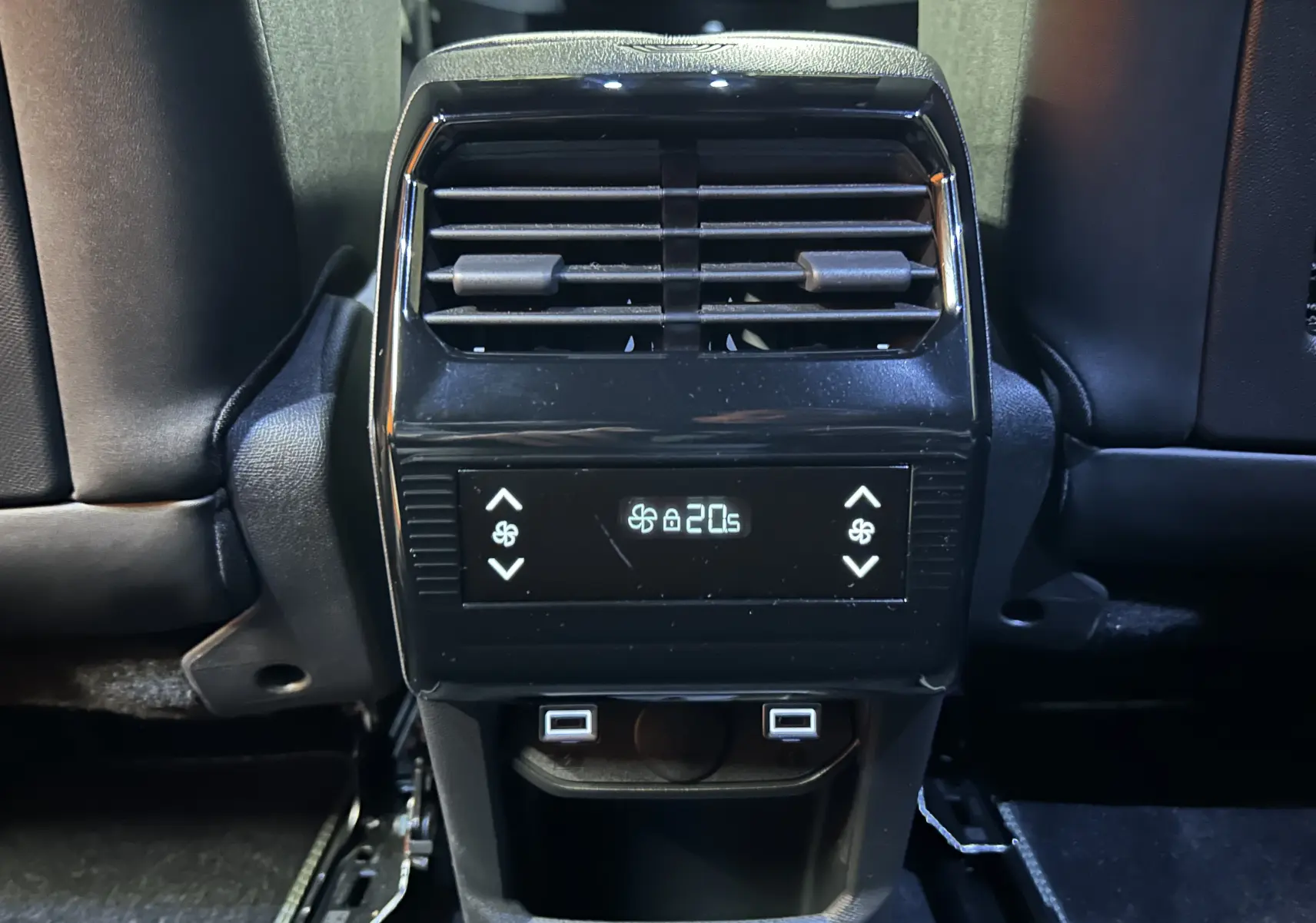 Vue rapprochée de la console arrière noire du Peugeot 5008 bleu Obsession, avec commandes climatisation et ports USB visibles.