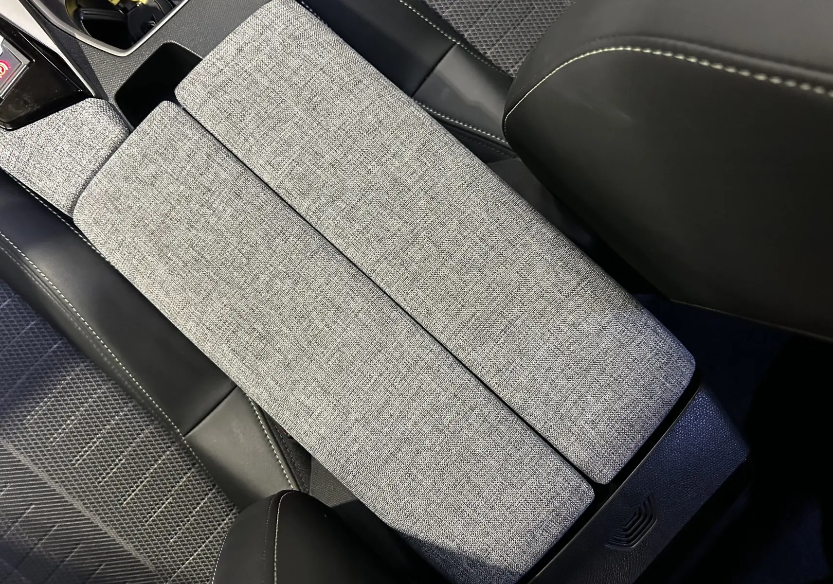 Détail de l'accoudoir central en tissu gris et cuir noir dans l'habitacle du Peugeot 5008 III Hybrid 145 GT.