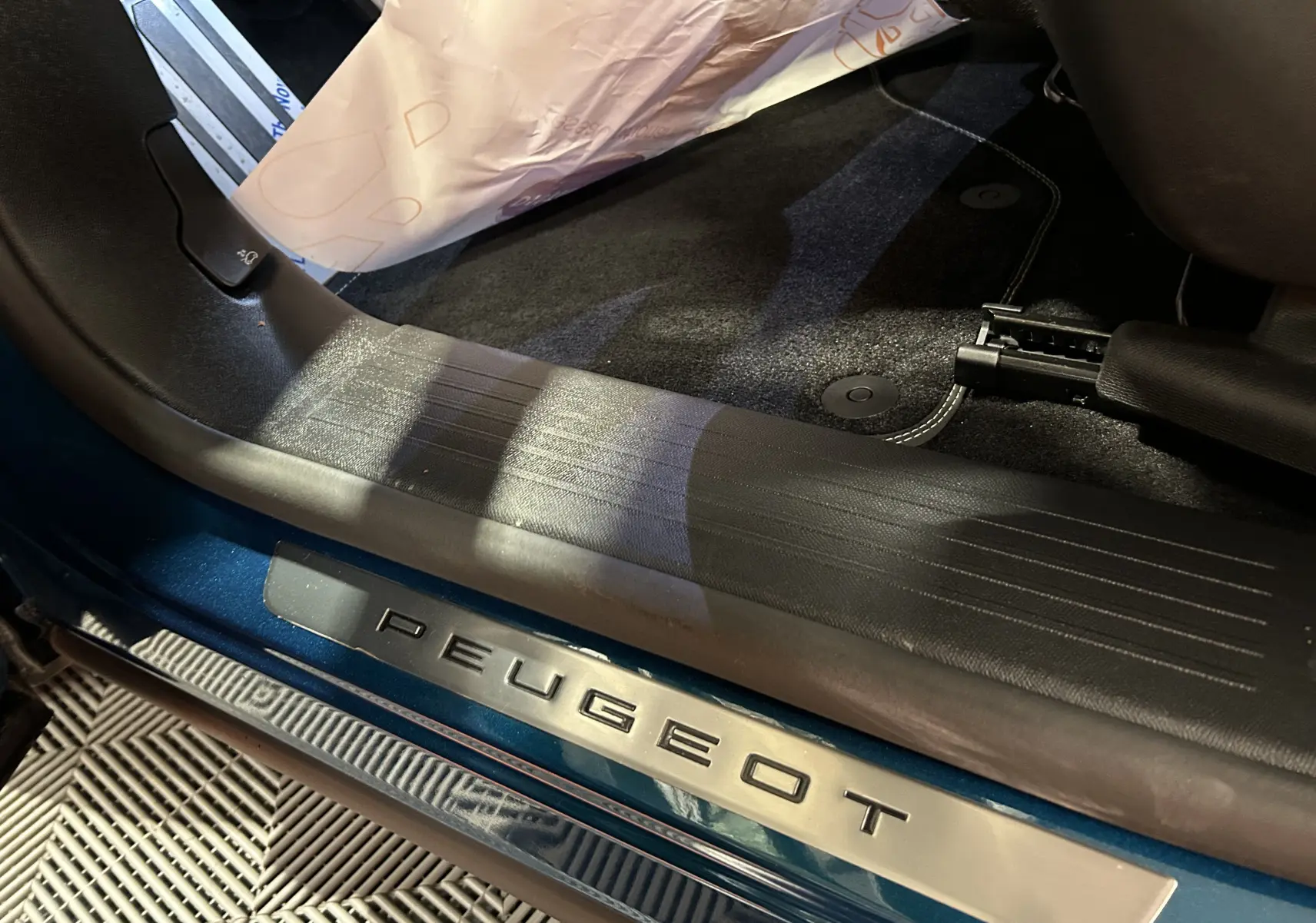 Gros plan sur le seuil de porte côté conducteur bleu obsession du Peugeot 5008 III Hybrid 145 e-DSC6 GT avec logo Peugeot.