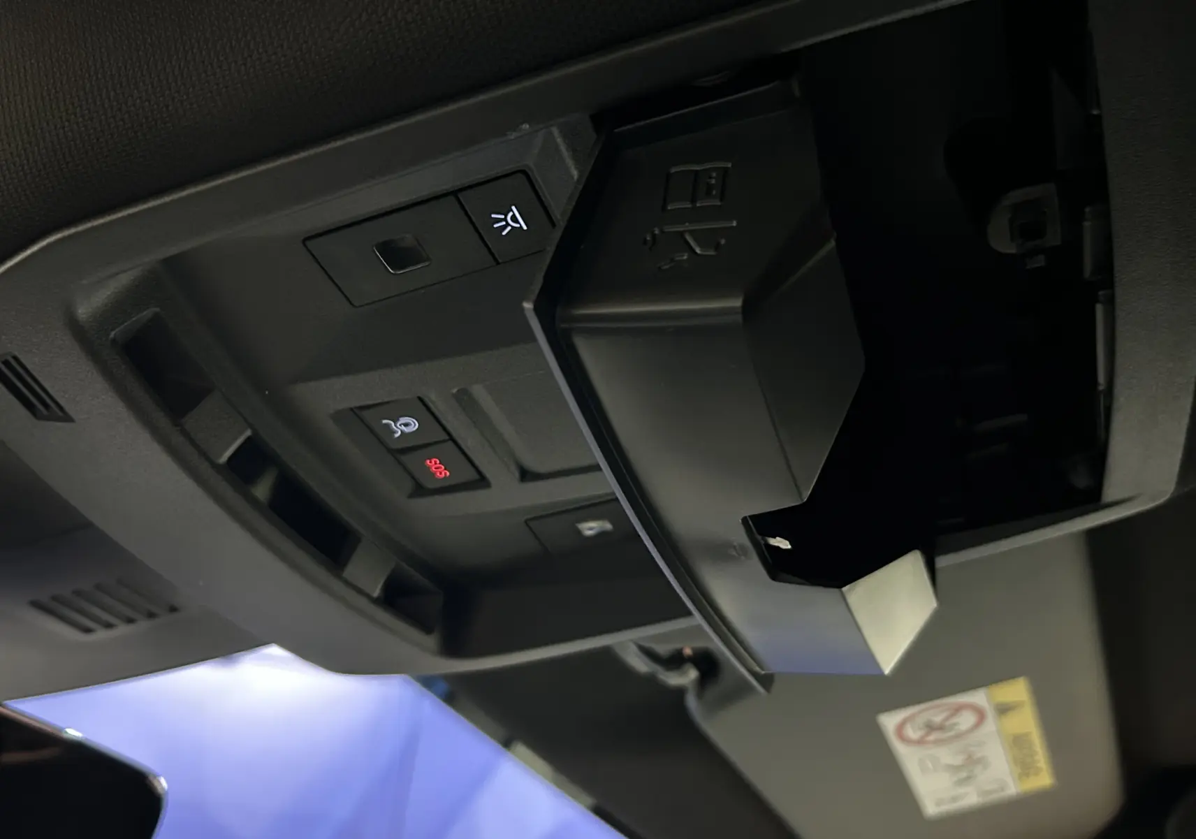 Gros plan sur le compartiment lunettes ouvert et les boutons de commande au plafond intérieur du Peugeot 5008 bleu obsession 2025.