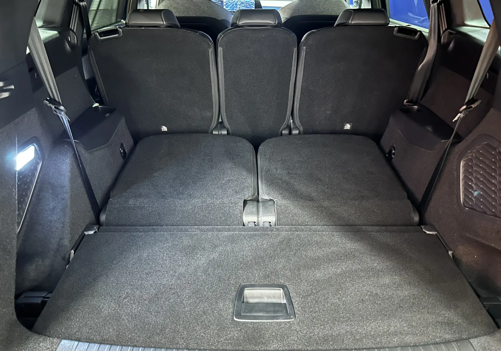 Coffre spacieux du Peugeot 5008 Hybrid 145 GT 2025, sièges arrière partiellement rabattus, intérieur noir.