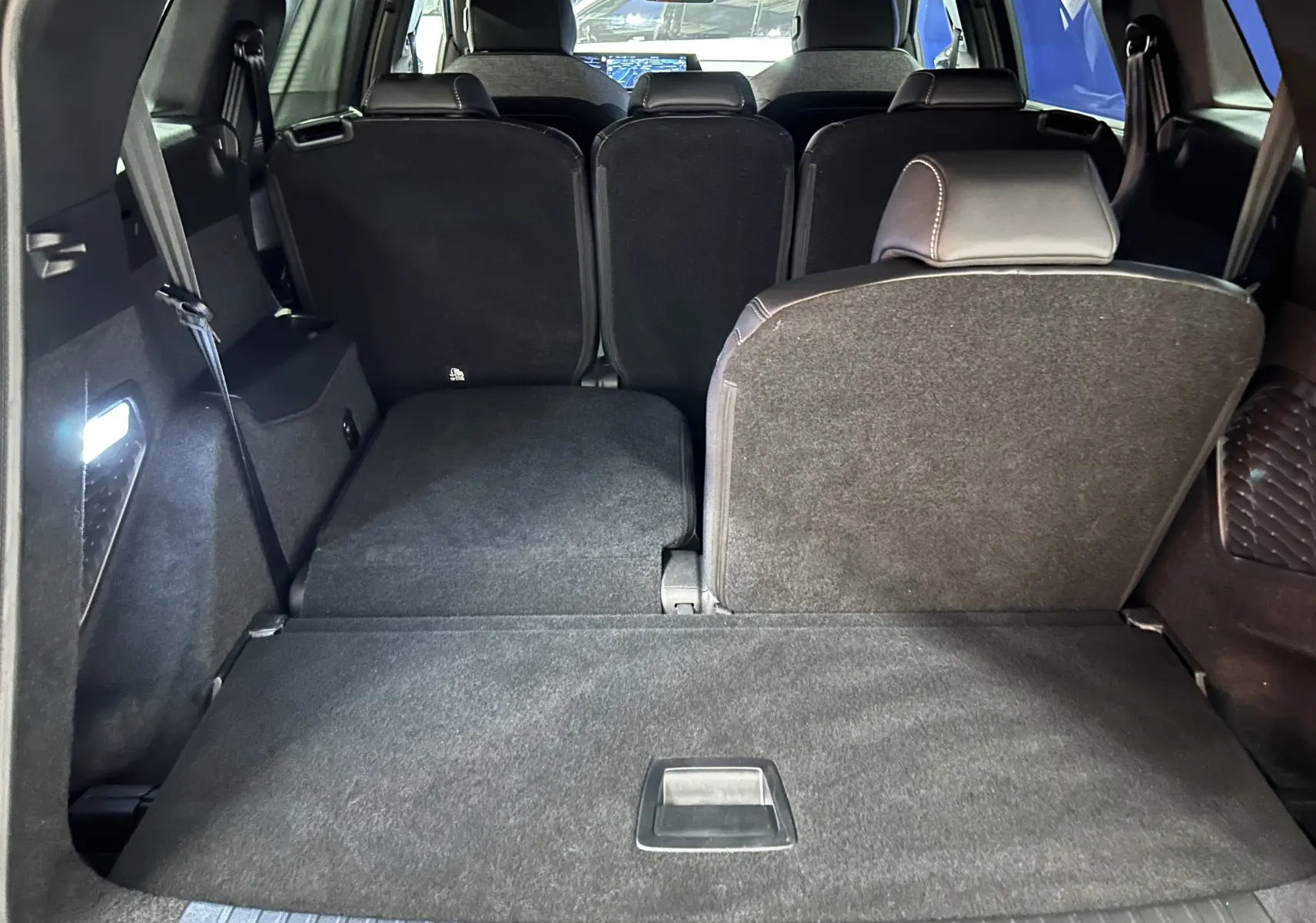 Vue arrière du coffre du Peugeot 5008 hybride 2025 bleu obsession avec sièges arrière partiellement rabattus et éclairage intérieur.