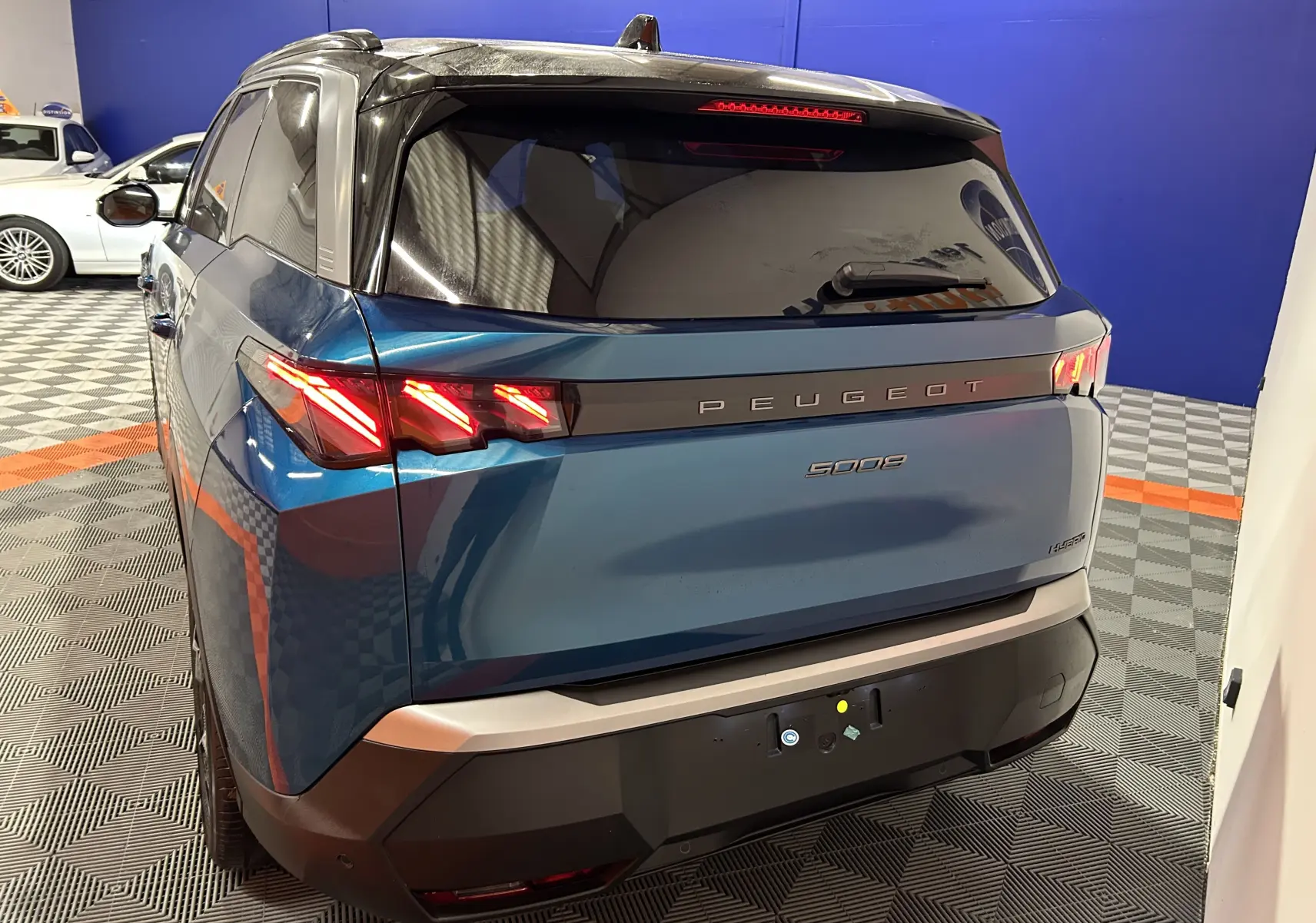Vue 3/4 arrière droite du Peugeot 5008 bleu obsession avec feux arrière LED allumés dans un showroom.