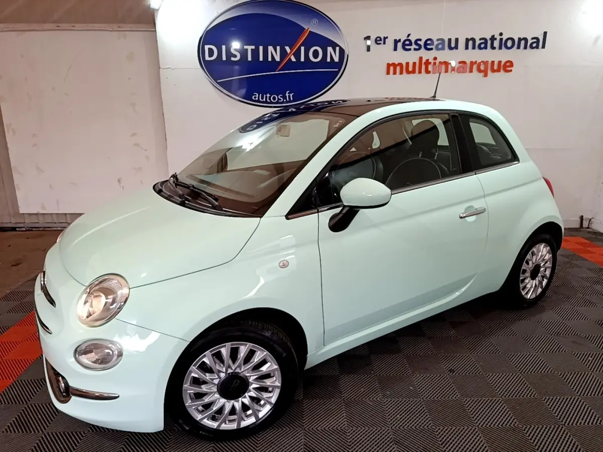 Vue 3/4 avant droite d'une Fiat 500 Lounge 2019 vert clair avec jantes alliage et phares allumés en intérieur showroom.