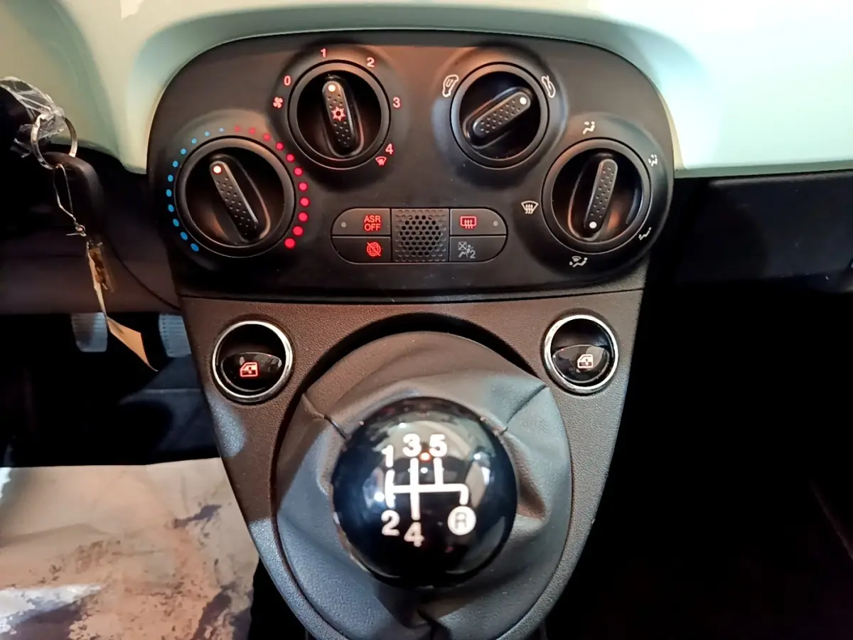 Gros plan sur la console centrale d'une FIAT 500 verte 2019, mettant en valeur le levier de vitesses manuel et les commandes de climatisation.