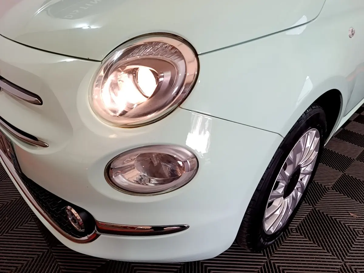 Gros plan sur l'avant droit vert clair d'une FIAT 500 1.2 8V 69ch Lounge avec phare allumé et jante alu.