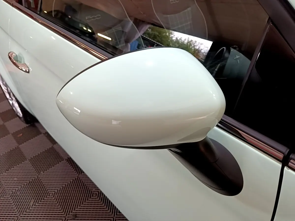 Gros plan sur le rétroviseur côté gauche blanc nacré d'une Fiat 500 Lounge 2019 avec porte assortie visible.
