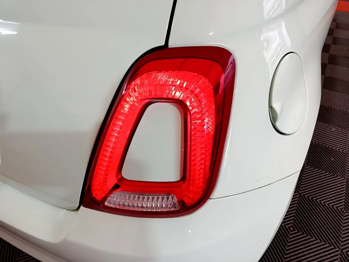 Gros plan sur le feu arrière droit rouge d'une FIAT 500 blanche, avec la trappe à carburant visible à côté.