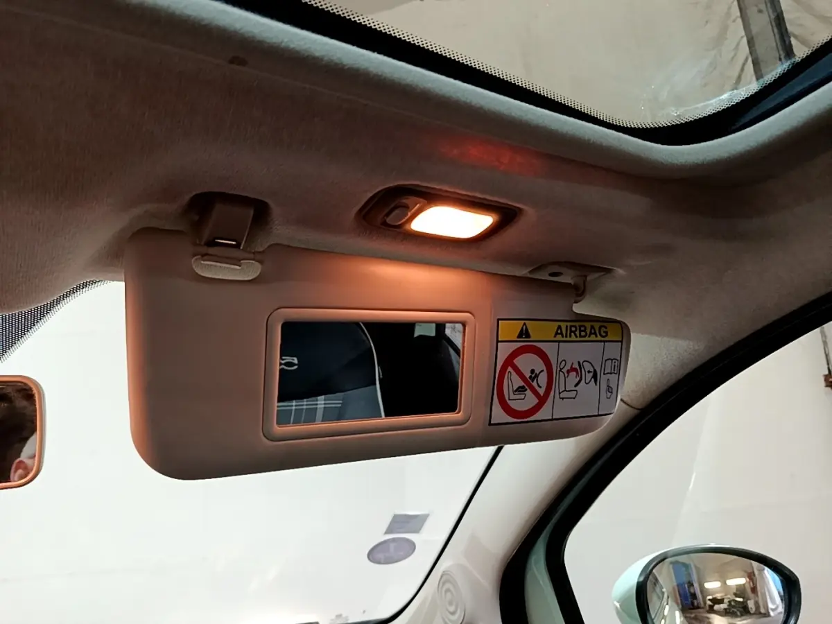 Détail du pare-soleil côté conducteur avec miroir éclairé et avertissement airbag dans l'habitacle clair d'une Fiat 500.