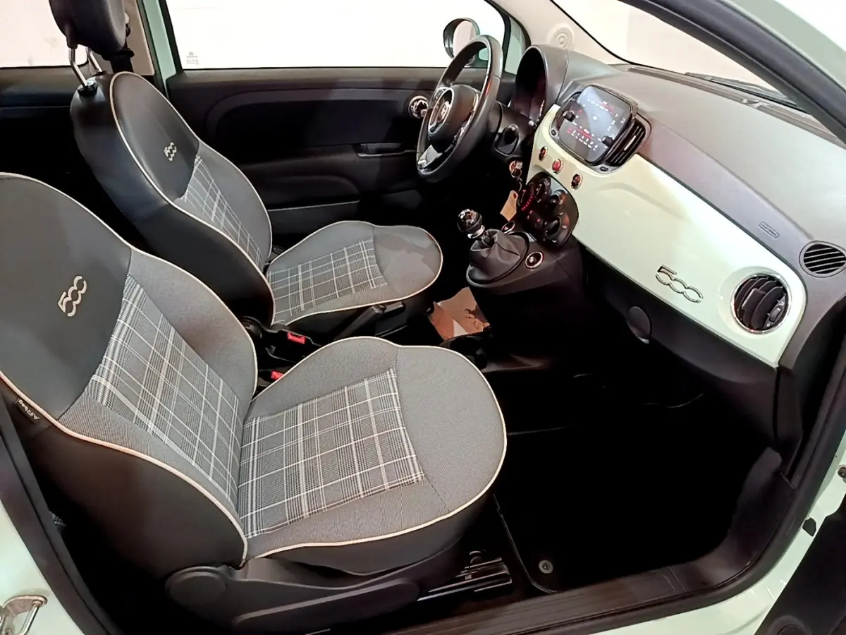 Vue intérieure côté conducteur de la Fiat 500 Lounge 2019, montrant les sièges gris à motif à carreaux et le tableau de bord clair.