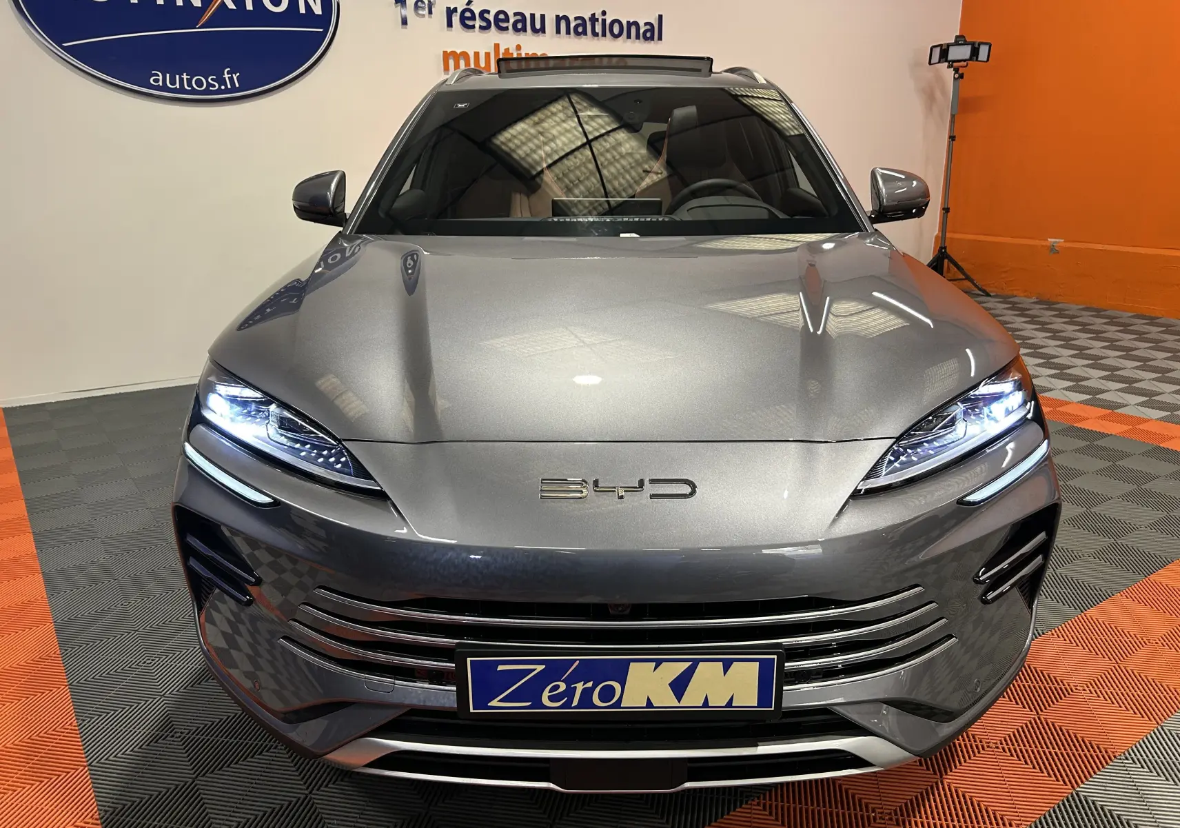 Vue frontale d'une BYD SEAL U grise métallisée avec phares LED allumés dans un showroom.