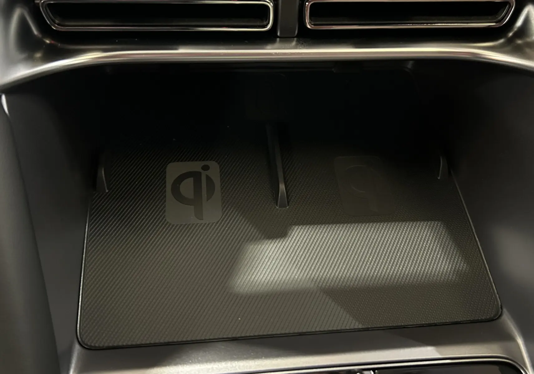 Gros plan sur le chargeur sans fil intérieur noir du BYD SEAL U 2025, avec logo Qi visible sous la console.