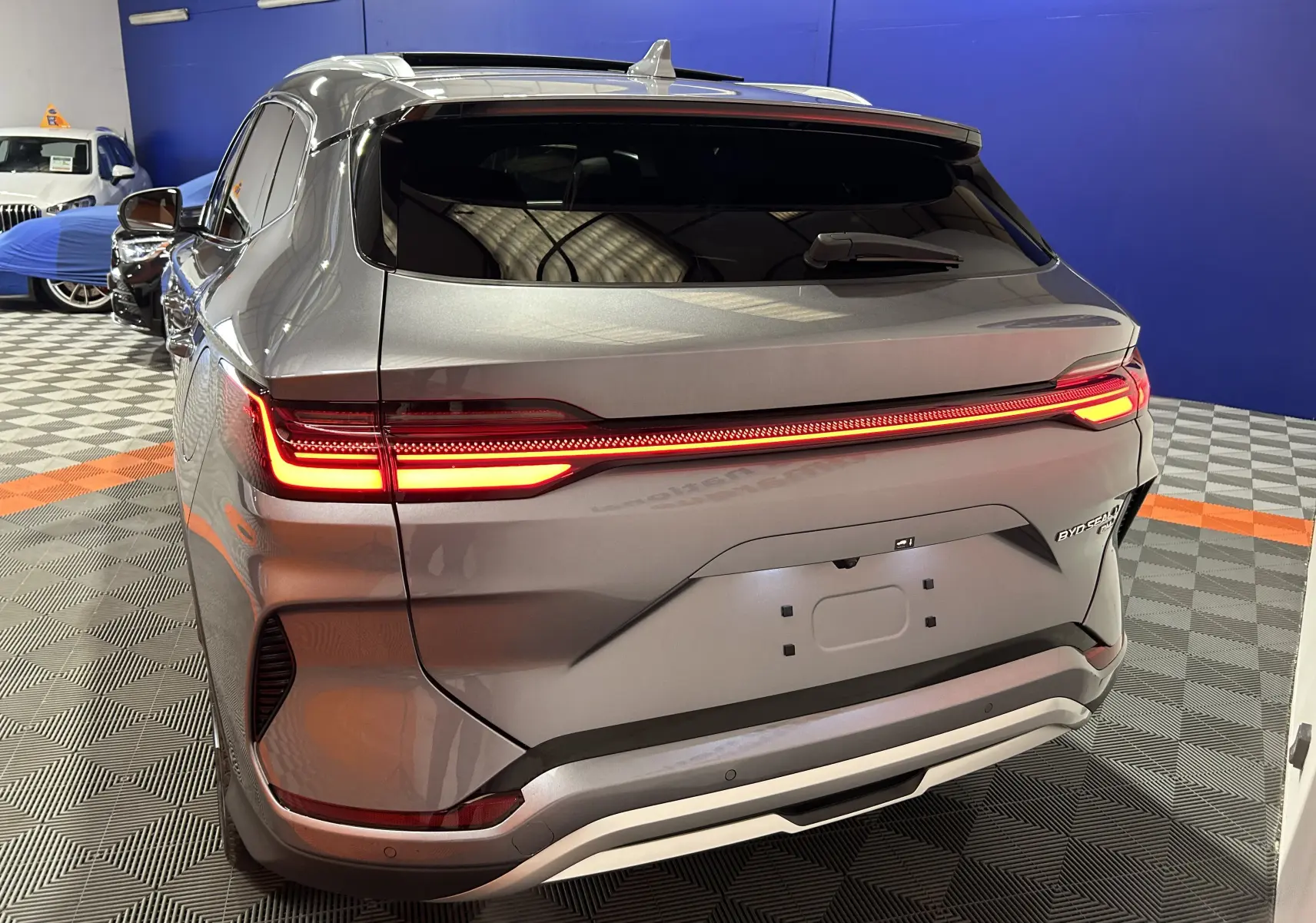 Vue 3/4 arrière droite du BYD SEAL U gris métallisé avec feux arrière allumés dans un showroom.