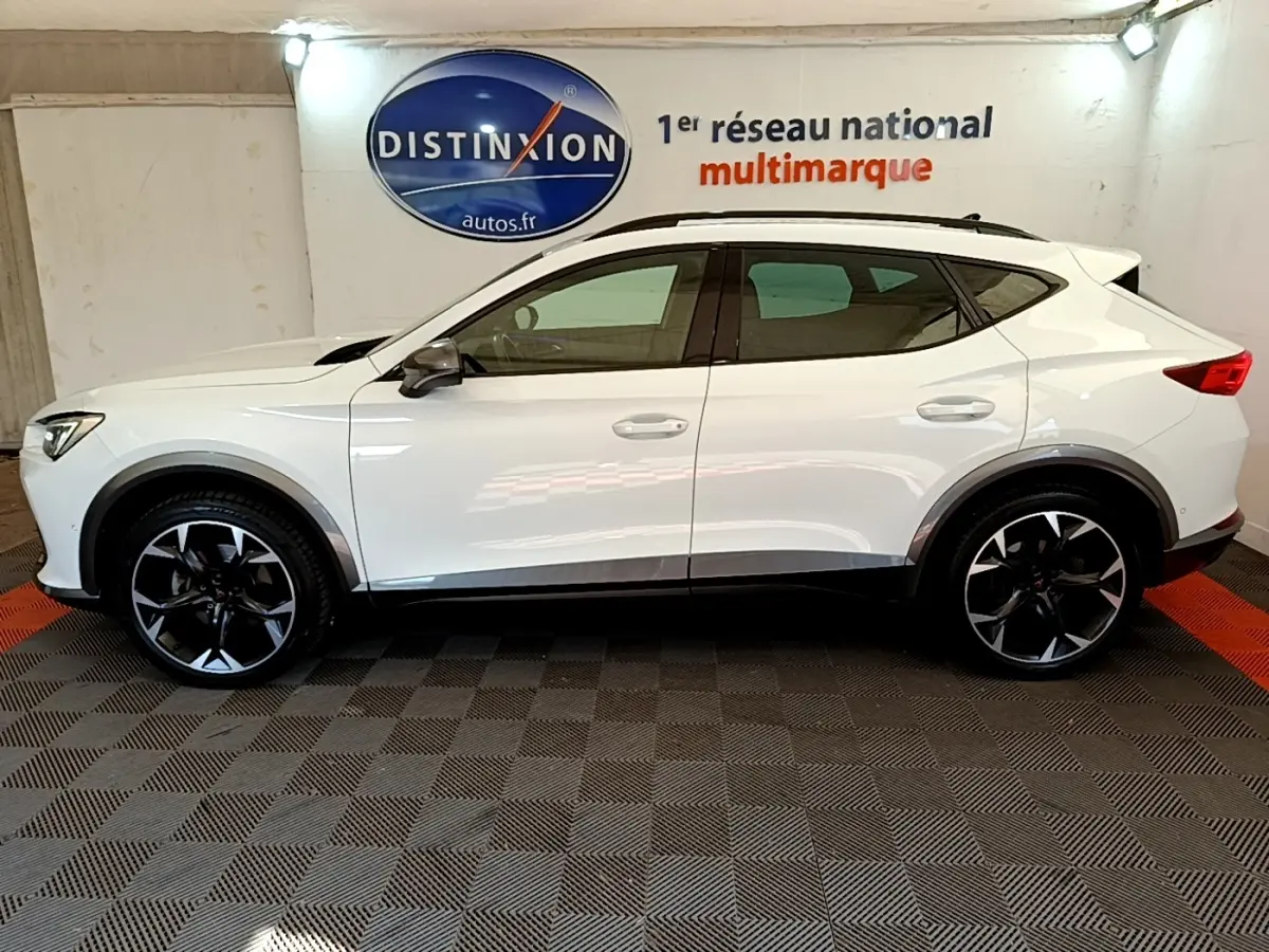 Profil droit d'un CUPRA Formentor blanc 2023 avec jantes noires et toit ouvrant, en intérieur showroom.