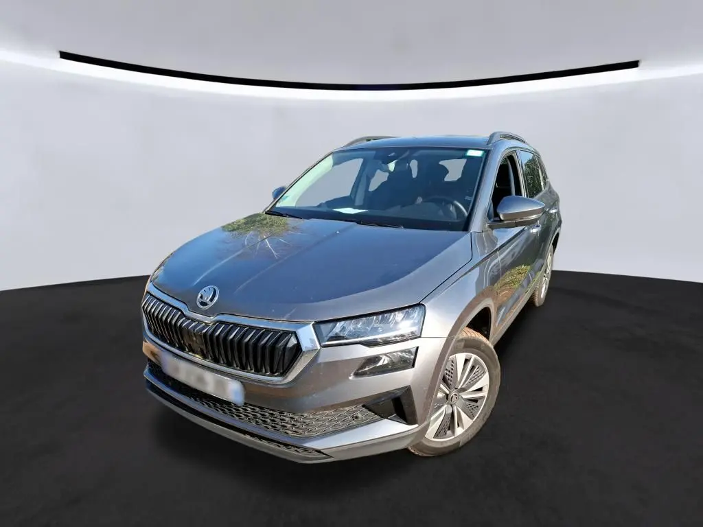 Vue 3/4 avant d'un Skoda Karoq gris métallisé avec calandre chromée et jantes alu 17 pouces sur fond neutre.