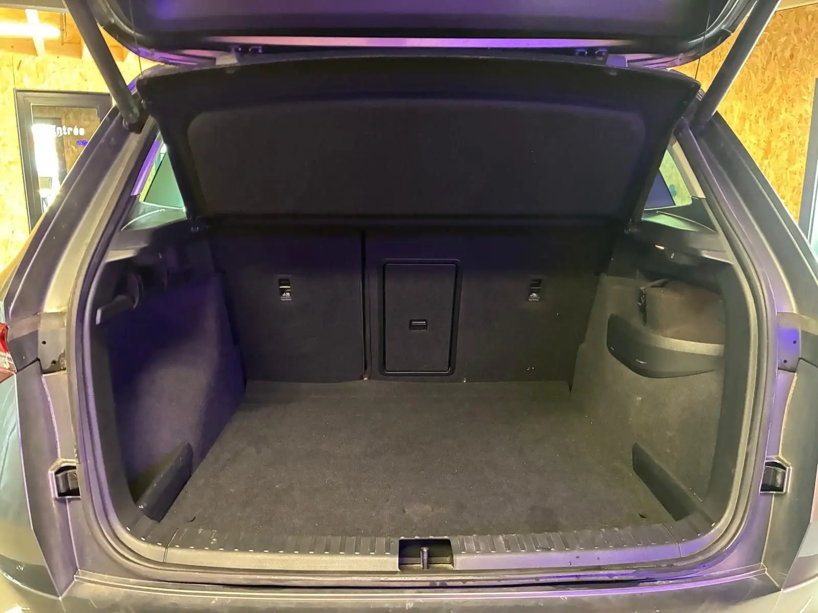 Coffre ouvert vu de l'arrière d'un Skoda Karoq gris 2023, espace de chargement vide et tapis noir.