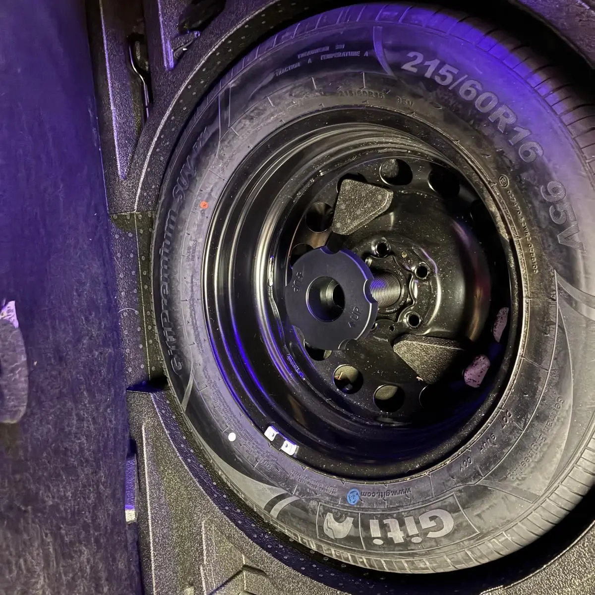 Gros plan sur la roue de secours noire dans le coffre d’un Skoda Karoq gris, vue de dessus.