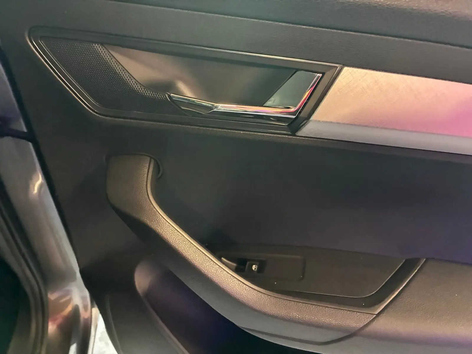 Détail de la poignée intérieure côté gauche d'une Skoda Karoq gris 2023 avec insert chromé et garniture noire.