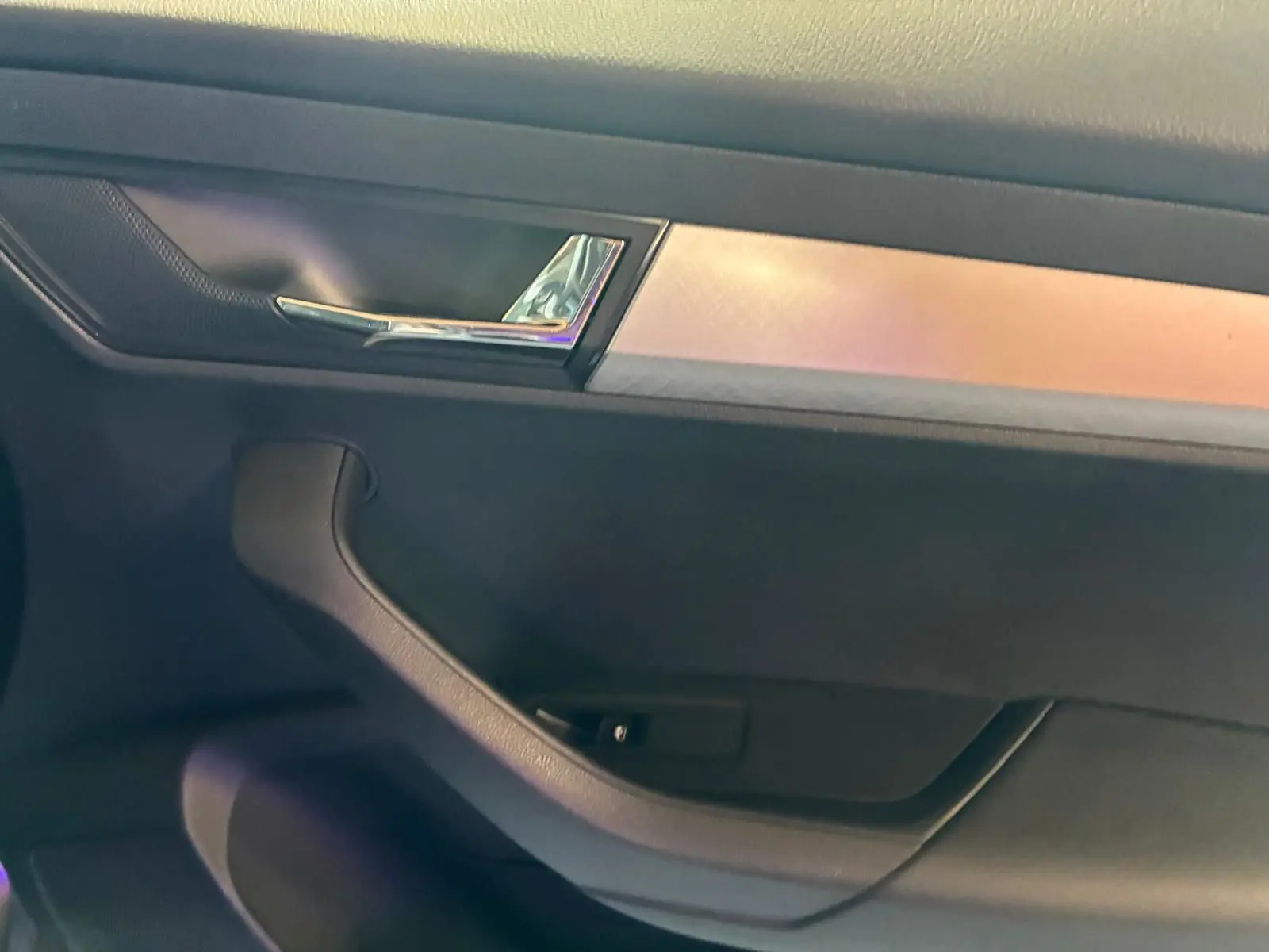Détail de la poignée intérieure et garniture noire avec insert chromé d'une porte côté gauche d'un Skoda Karoq gris.