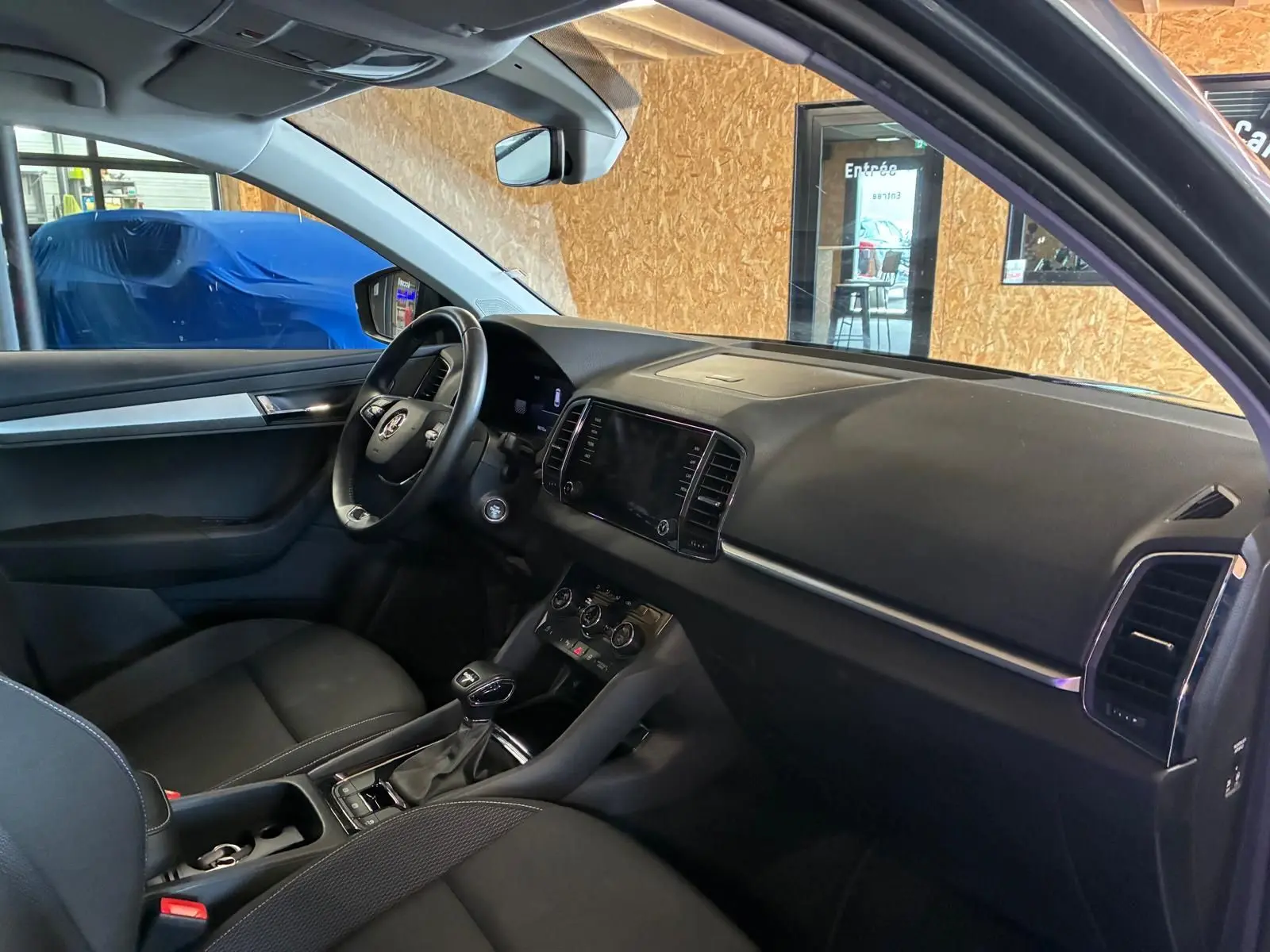 Vue intérieure côté conducteur du Skoda Karoq gris 2023, avec tableau de bord noir et volant multifonctions.