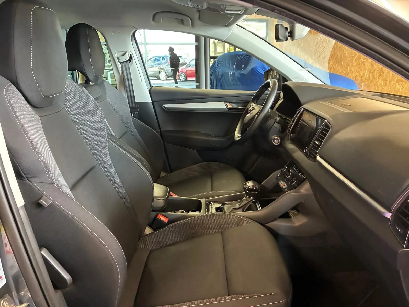 Intérieur avant du Skoda Karoq gris 2023, vue côté conducteur, sièges noirs et tableau de bord moderne.