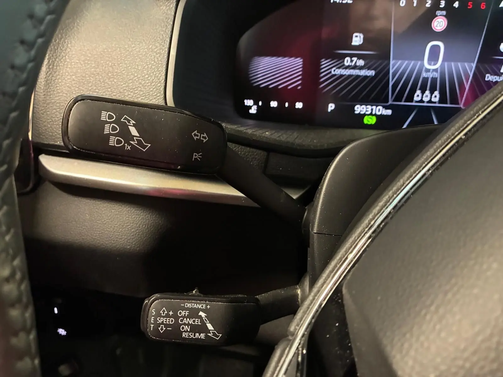 Gros plan sur les commandes au volant d’un Skoda Karoq 2.0 TDI gris, affichage numérique du tableau de bord en arrière-plan.